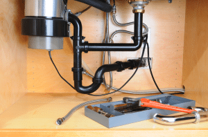 Garbage disposal unit installed under kitchen sink with plumbing components and tools visible, highlighting home waste management solutions.