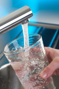 Hand filling a glass with clean drinking water from a modern faucet, emphasizing the importance of water filtration for health and safety.