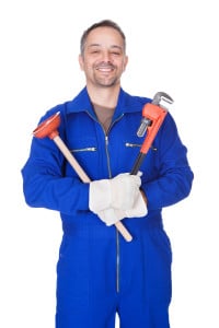 Smiling plumber in blue uniform holding a plunger and a pipe wrench, representing professional plumbing services and solutions for discolored water issues.