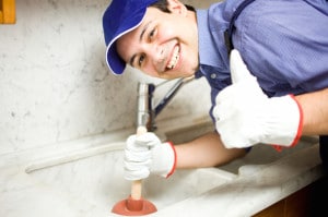Plumber using a plunger to clear a clogged sink, smiling and giving a thumbs-up, representing professional drain cleaning services.