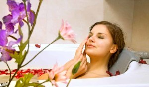 Woman relaxing in a luxurious bathtub surrounded by flower petals and decorative plants, illustrating a serene bathroom atmosphere ideal for remodeling and relaxation.