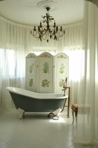 Elegant bathroom featuring a vintage clawfoot bathtub, decorative folding screen with floral designs, and a chandelier, emphasizing a luxurious and inviting atmosphere for bathroom remodeling.