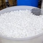 Round plastic container with small white spheres in an industrial setting, representing organized plumbing supplies storage.