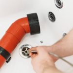 Person's hand using a tool on a red drainage pipe during plumbing maintenance for Allore's Plumbing Services LLC.