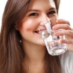 Young woman enjoying a clear glass of water, promoting hydration and wellness for effective plumbing maintenance.