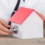 Model house with red roof and white walls, featuring a hand holding a stethoscope related to Allore's Plumbing Services.