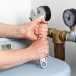 Hands with an adjustable wrench on a water heater pressure gauge by Allore's Plumbing Services LLC.