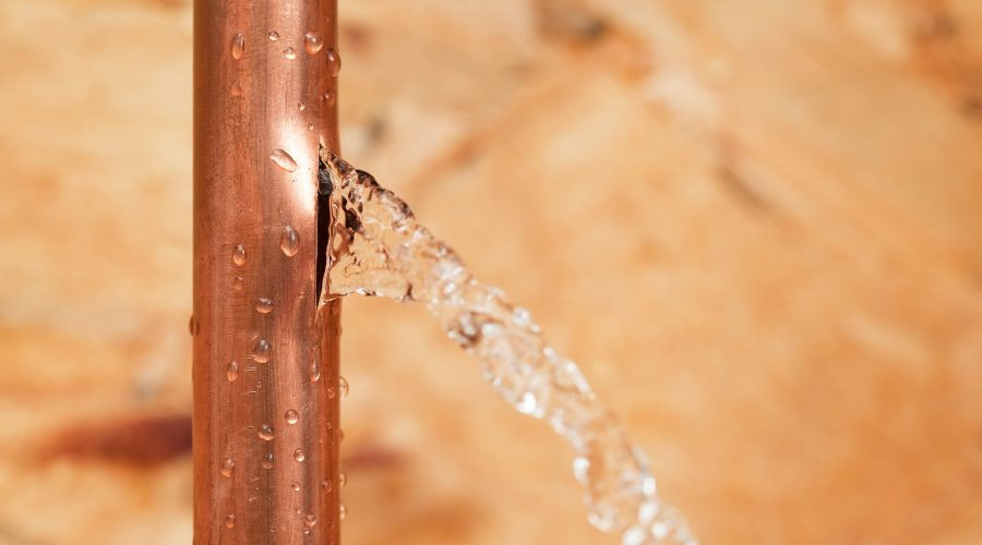 Copper pipe with visible water leak and droplets, highlighting signs of plumbing issues related to water leaks and potential damage.
