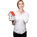 Woman holding a small model house, contemplating real estate decisions related to plumbing services in Stuart, FL.