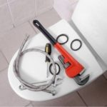 Image of plumbing tools on a toilet, including an adjustable wrench and plumbing hose, arranged for holiday maintenance tips.