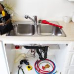 Double sink with faucet, plumbing tools, and maintenance supplies underneath, illustrating plumbing system upkeep and repair services offered by Allore's Plumbing in Stuart, FL.