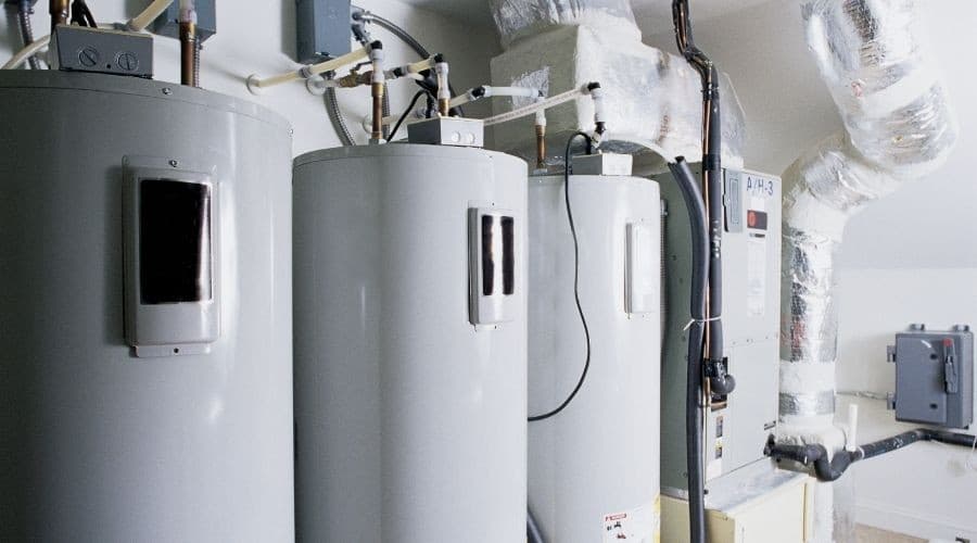 Three gray hot water heaters and insulated piping by Allore's Plumbing Services LLC.