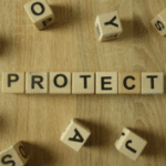Scrabble-like tiles spelling 'PROTECT' on a wooden surface related to plumbing services by Allore's Plumbing.
