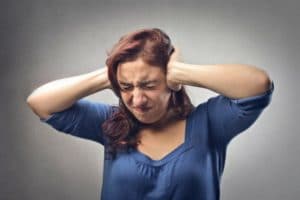 Woman with red hair covering her ears, expressing distress from unwanted noise, related to plumbing issues and clogged drains.