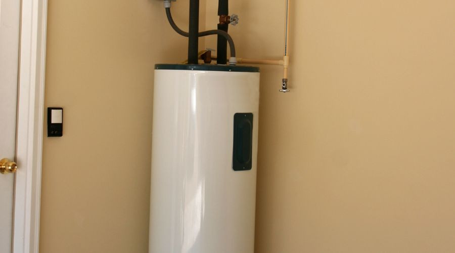 Water heater with pipes and valves, installed against a beige wall by Allore's Plumbing Services LLC.