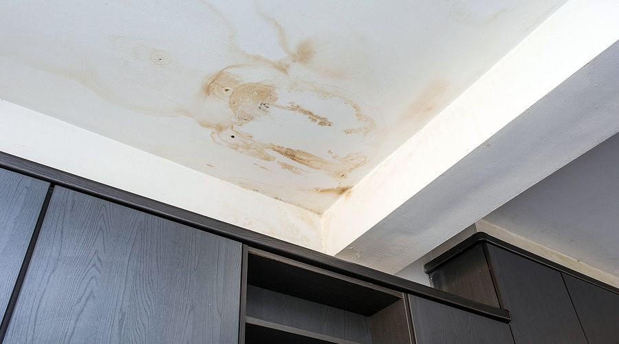 Water-damaged ceiling with stains near dark cabinetry; plumbing issues by Allore's Plumbing Services LLC.