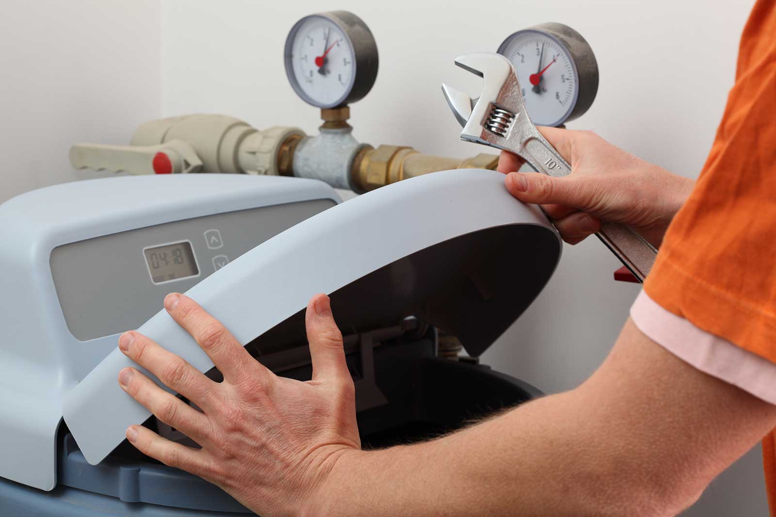 Person using an adjustable wrench on a machine with pressure gauges in an industrial setting for plumbing repair services.