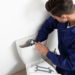 Male plumber in work attire servicing a toilet tank with tools for Allore's Plumbing Services LLC.