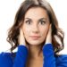 Woman with brown hair in blue top covering ears on plain white background. Image related to plumbing services.