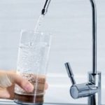 Modern tap faucet pouring water into a clear glass held by a hand, related to Allore's Plumbing Services LLC.