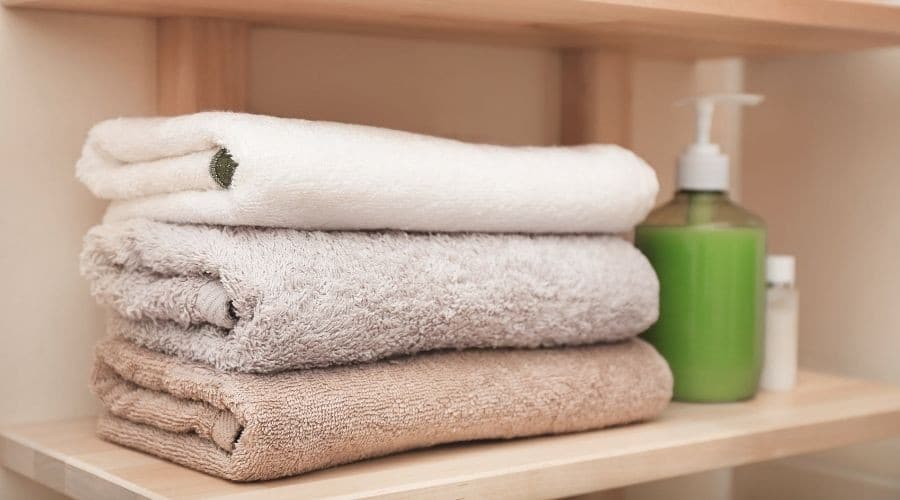 Towels stacked neatly on a wooden shelf, with a soap dispenser and bottle, promoting cleanliness for plumbing service users.