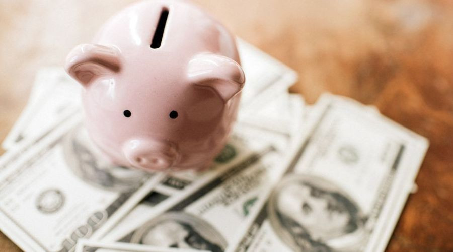 Pink piggy bank with stacks of hundred-dollar bills, representing financial planning for plumbing service needs.