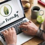 Hands typing on a laptop with an "Eco Friendly" logo, coffee cup, fruit bowl, and apple, emphasizing plumbing service advice.