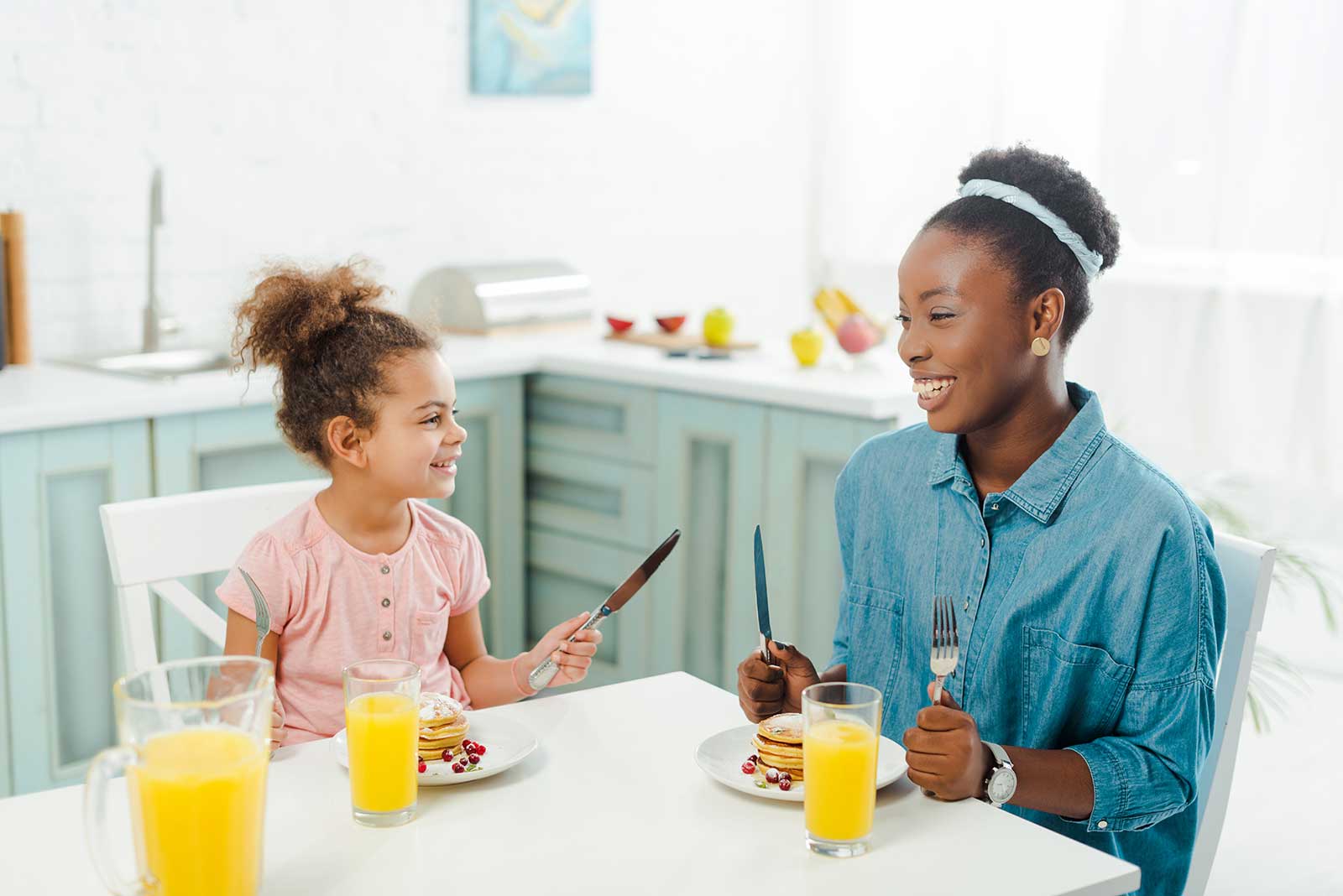 Woman and girl enjoying breakfast with pancakes and juice in a bright kitchen, showcasing family time and home comfort.