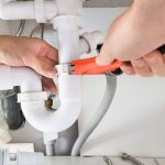 Hands adjusting white PVC pipes with an adjustable wrench during plumbing work by Allore's Plumbing Services LLC.