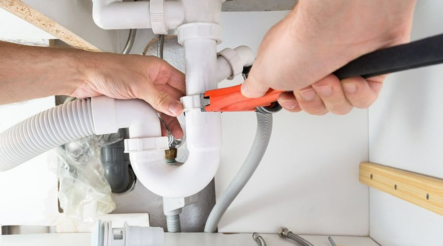 Human hands using a pipe wrench on plumbing components, showcasing Allore's Plumbing Services LLC expertise in repairs.