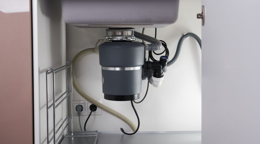 Gray garbage disposal unit installed under kitchen sink, integrated with plumbing, by Allore's Plumbing Services LLC.