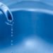 Close-up of a water faucet flowing into a blue basin, with drips highlighting plumbing maintenance.