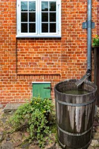 Rain barrel collection system beside brick wall, promoting water conservation in arid climates and addressing water shortages.