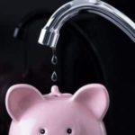 Sleek chrome faucet with water droplets above a pink piggy bank, illustrating plumbing advice on dripping faucets.