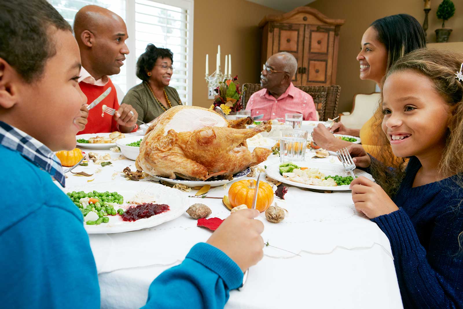 Family gathering around a dining table with Thanksgiving turkey and side dishes, showcasing joyful interactions and warmth.